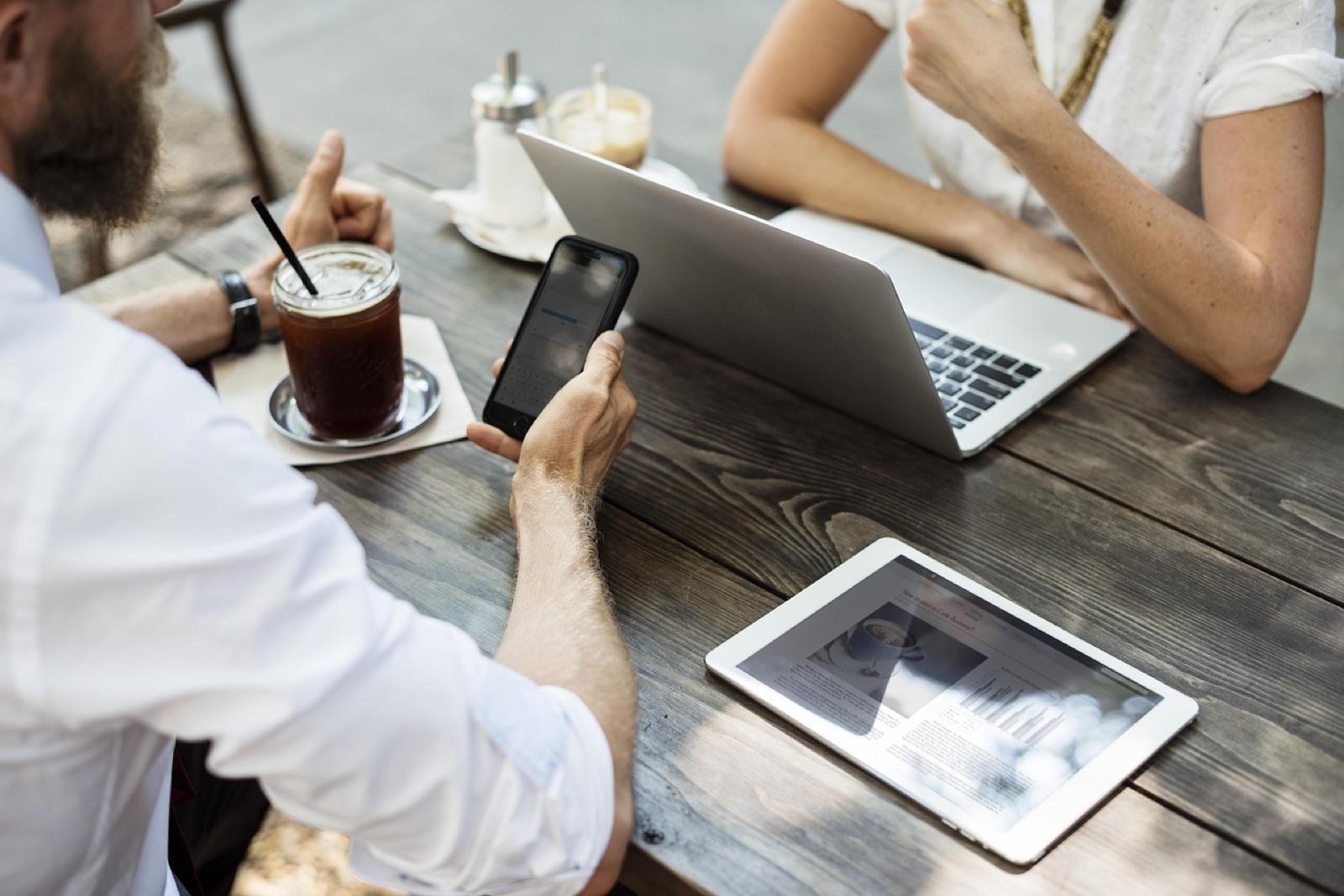Two people at a café table with a laptop, smartphone, tablet and coffee