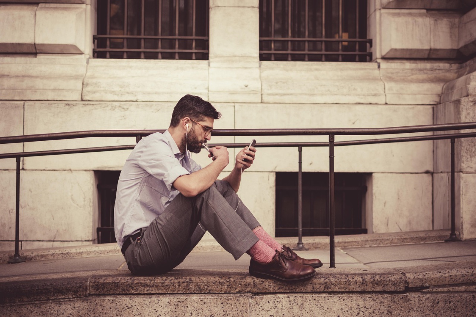 Man sitting on a stone ledge outside a building looking at his smartphone