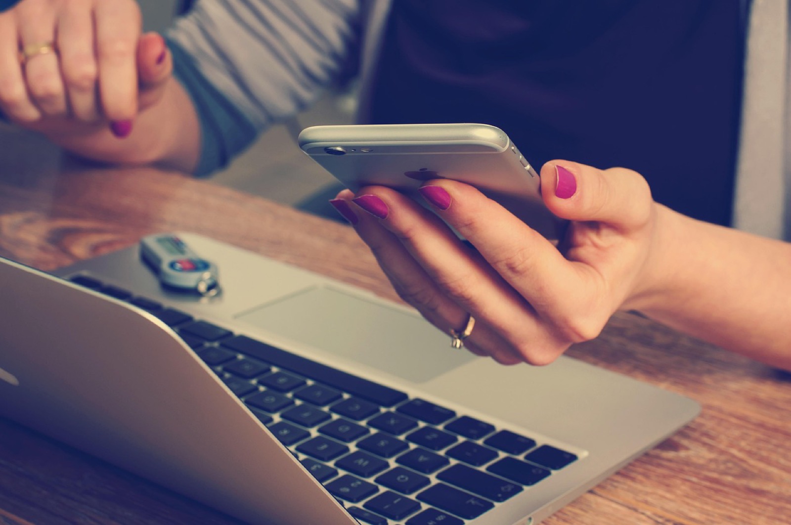 Woman holding a smartphone over a laptop on a wooden desk