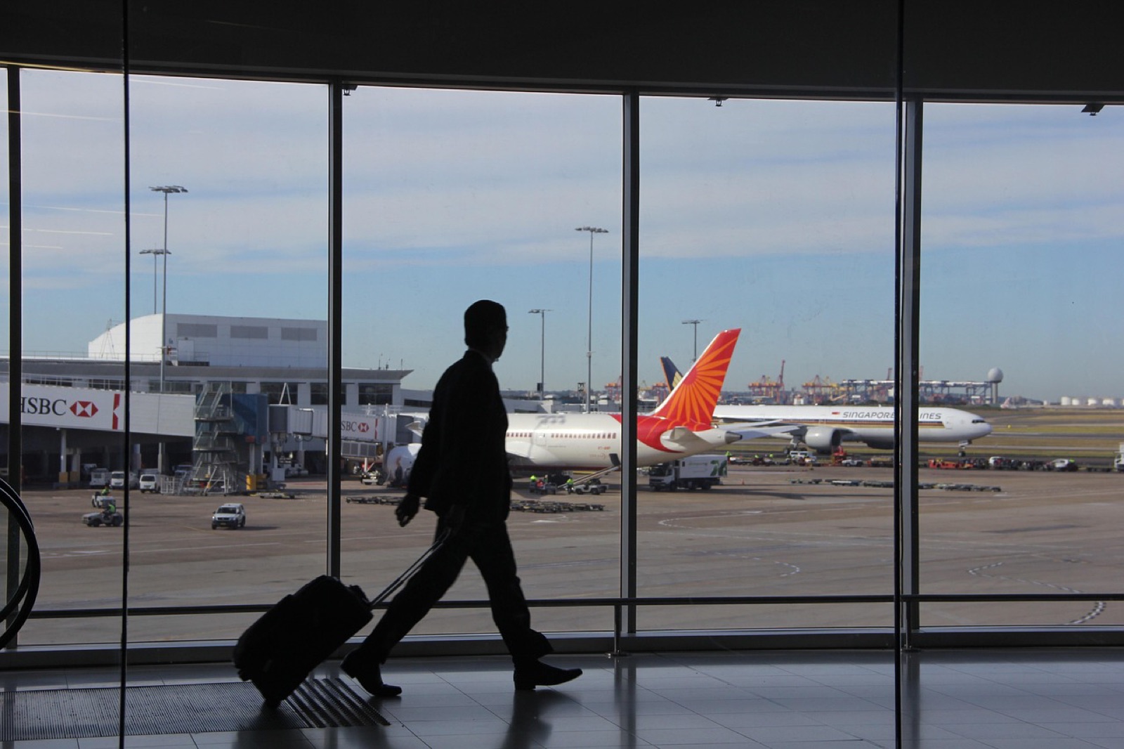 Silhouette of a traveler pulling a suitcase past airport windows with a parked airliner outside