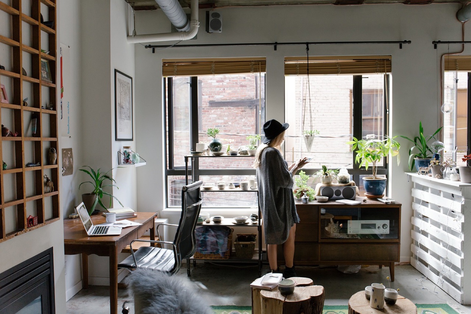Person standing at the window of a bright home office with plants and bookshelves