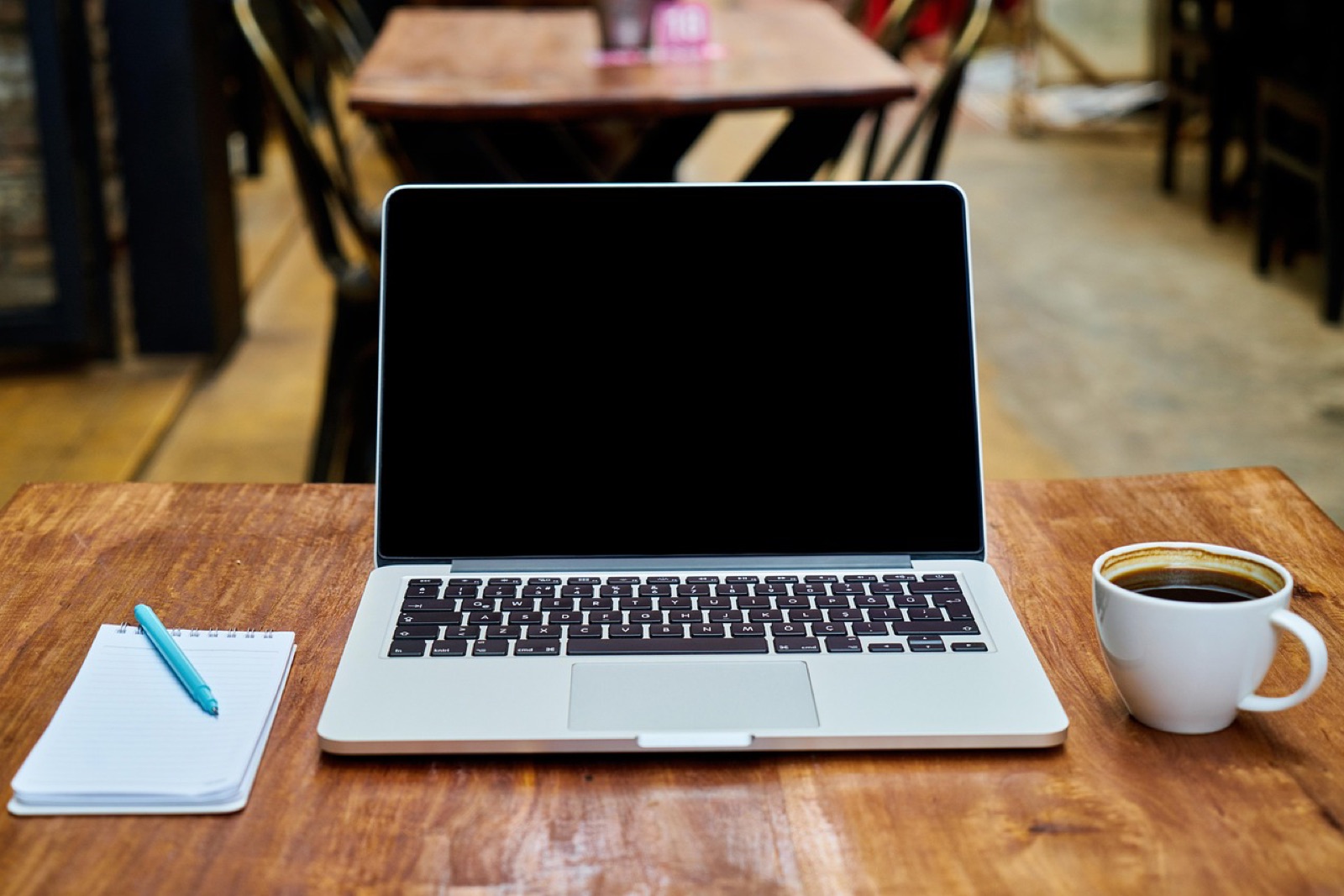 Laptop, notebook and a cup of coffee on a wooden café table