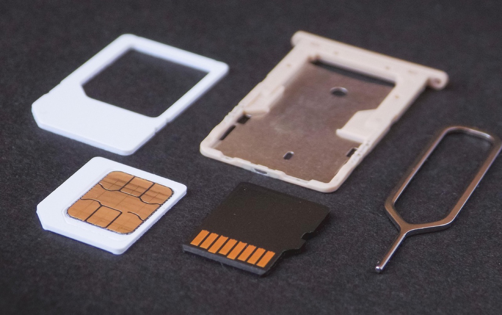 SIM card adapter, nano SIM, memory card, SIM tray and ejector pin on a gray surface