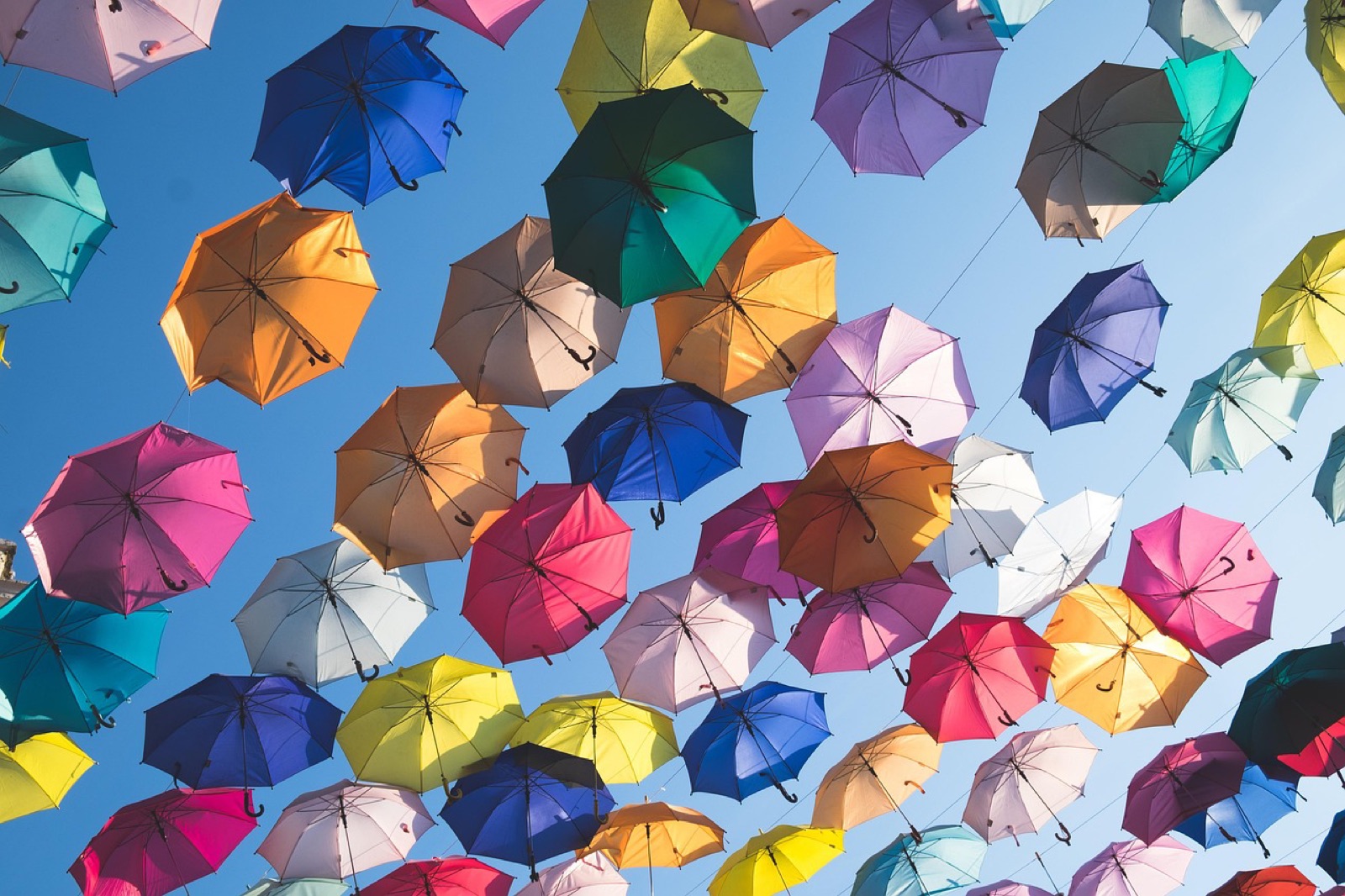 Rows of colorful open umbrellas strung above a street against a blue sky