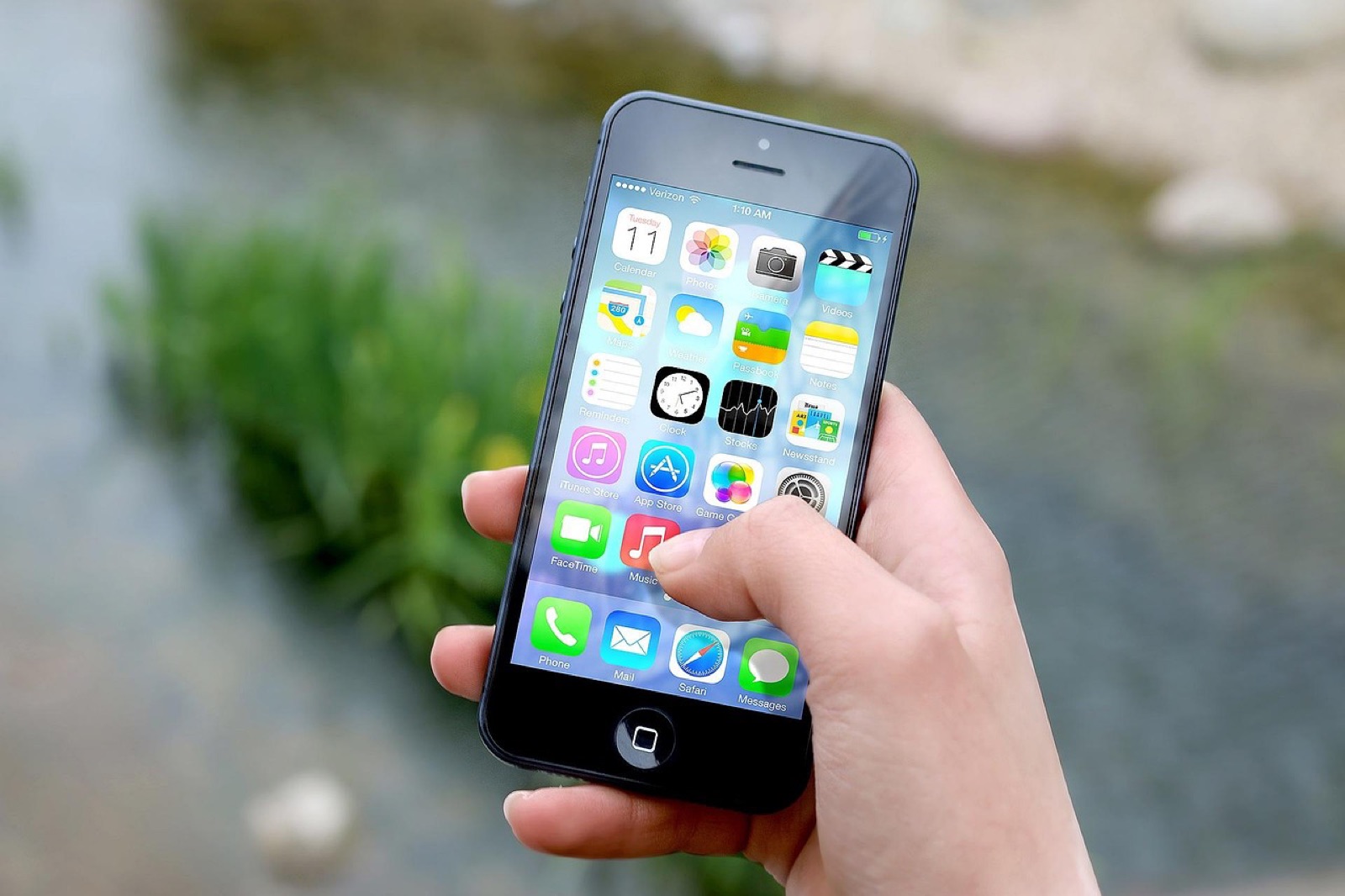 Hand holding a smartphone showing its home screen of apps