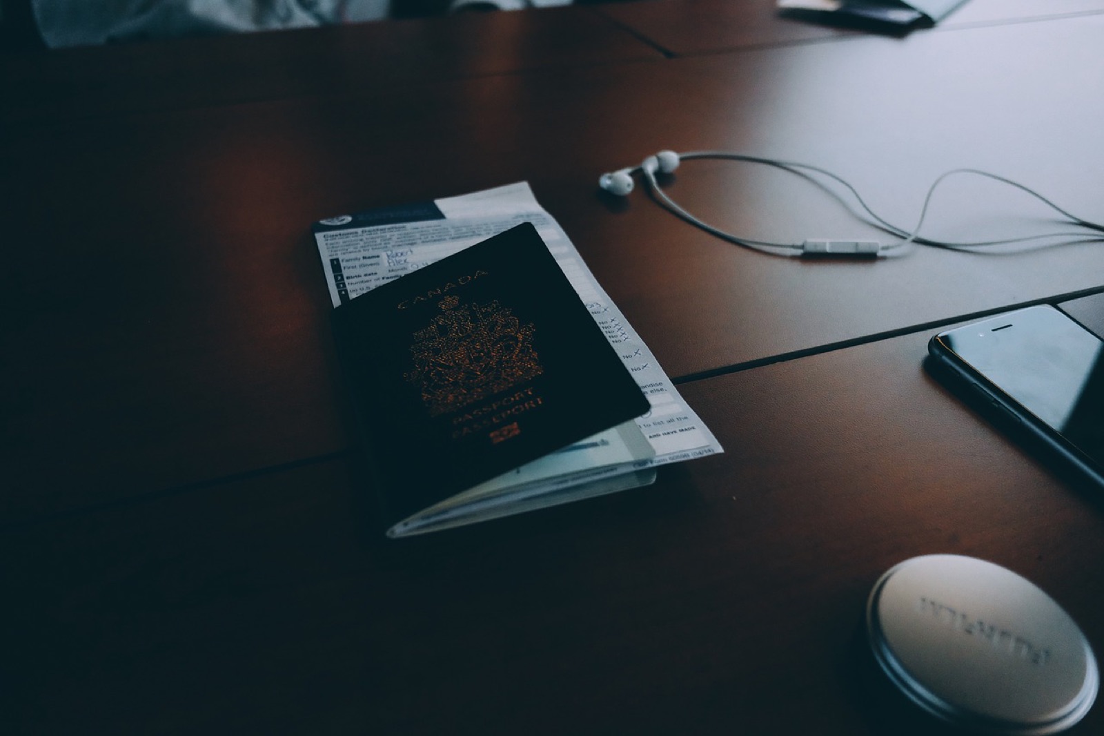 Passport and earphones on a dark wooden table beside a smartphone