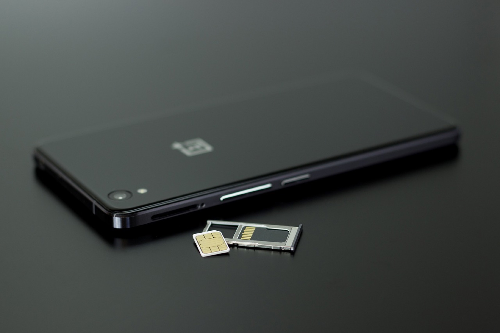 Black smartphone lying beside its removed SIM tray and SIM card
